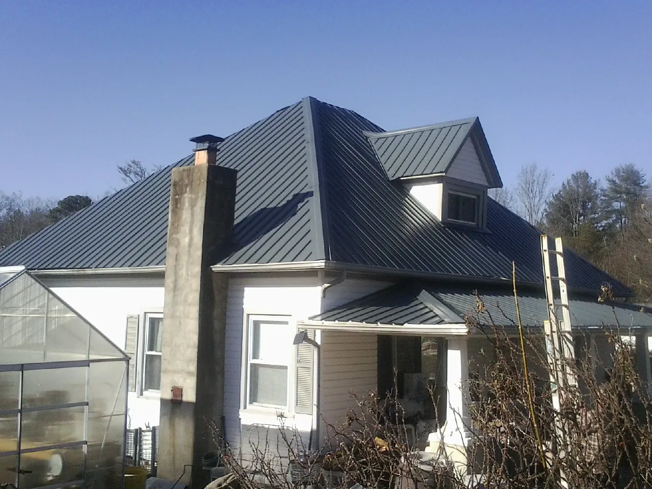 Dark blue standing seam metal roof on a white farmhouse with dormer — Slate & Tile Roof Repair by Roofing Brothers in Cashton