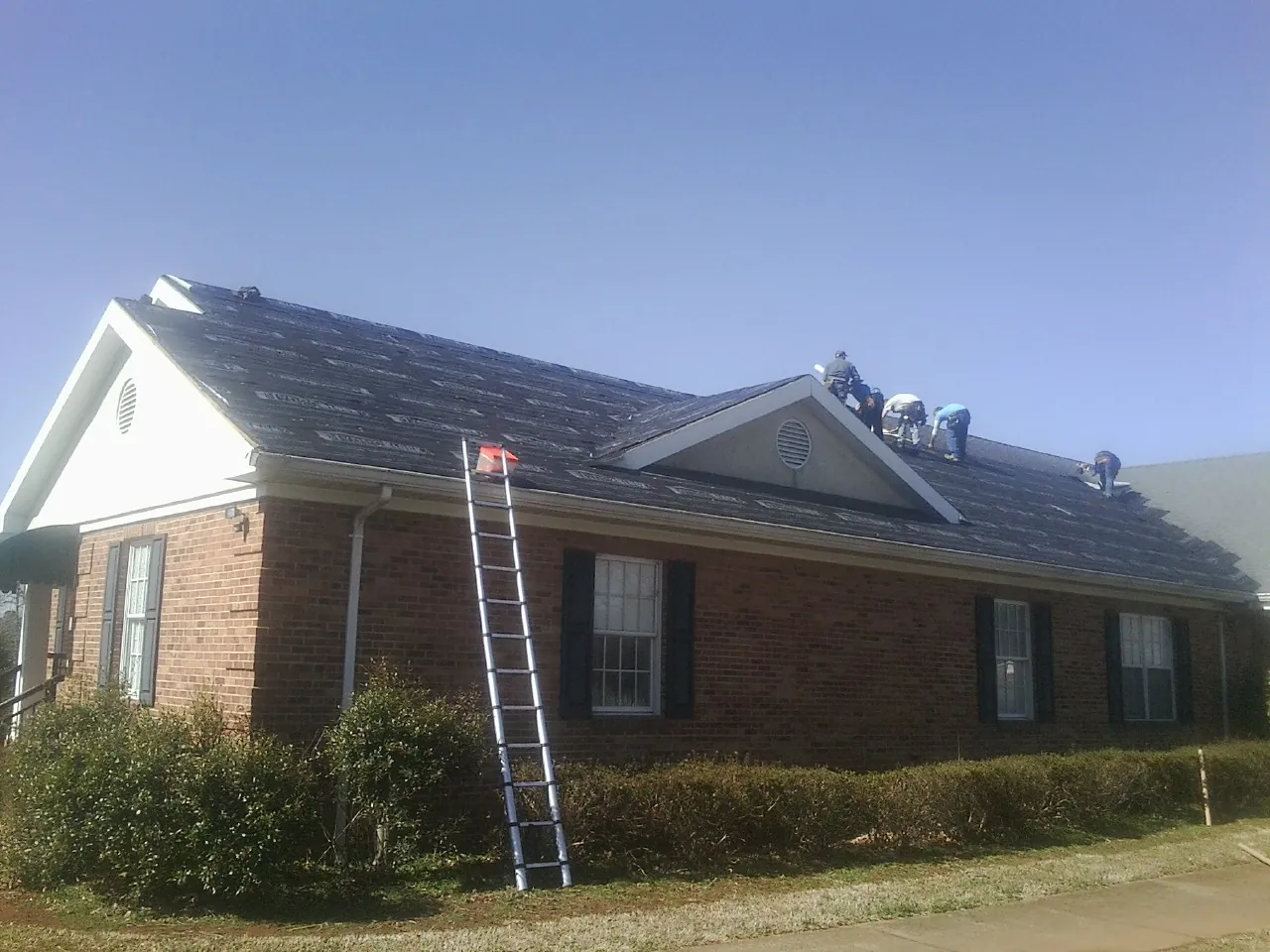 Crew tearing shingles off a brick ranch roof with a ladder set — Metal Roof Repair work by our crew in Cashton