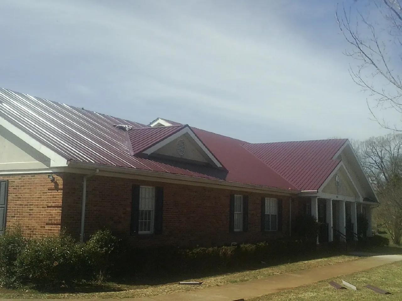 Red metal roof with gabled entries on a long brick building, from a Hail Damage Roof Repair job in Cashton