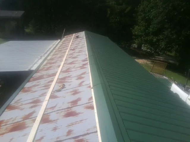 Old rusted panels beside newly installed green metal roofing — Wind Damage Roof Repair by Roofing Brothers in Cashton