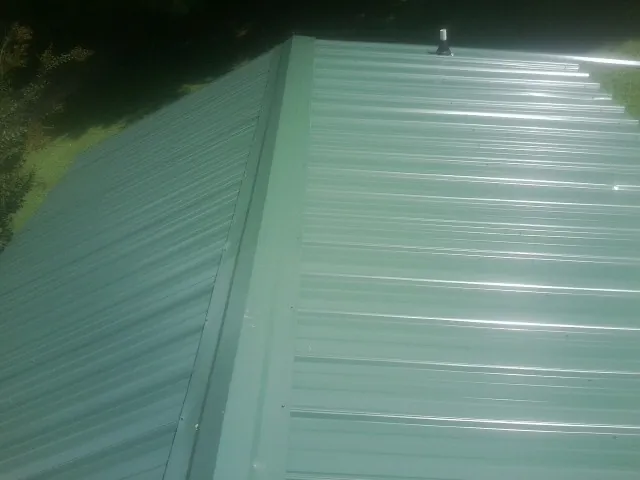 New green metal panels meeting at the ridge of a roof — Flat Roof Repair work by our crew in Cashton