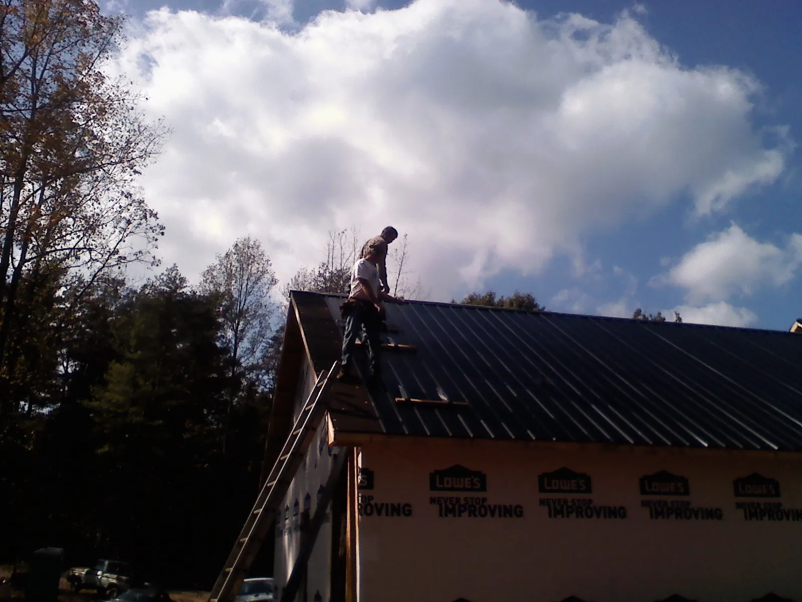 Roofer fastening dark metal panels high against a cloudy sky, from a Roof Inspection job in Cashton