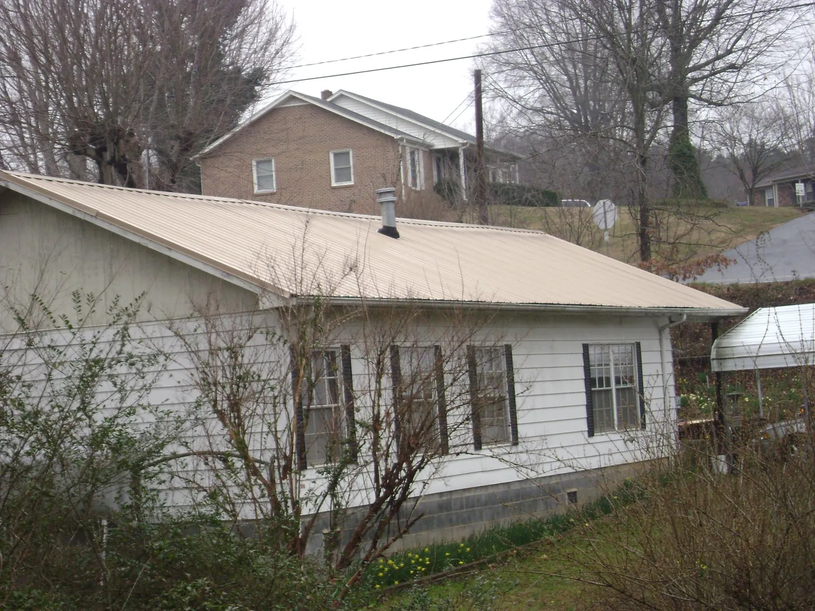 Tan metal roof on a white sided house set into a hillside — Commercial Roofing by Roofing Brothers in Cashton